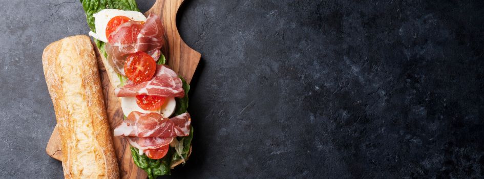 Φρέσκο ιταλικό Panino με προσούτο, μοッツαρέλα, ντομάτα και μαρούλι πάνω σε ξύλινη επιφάνεια κοπής.